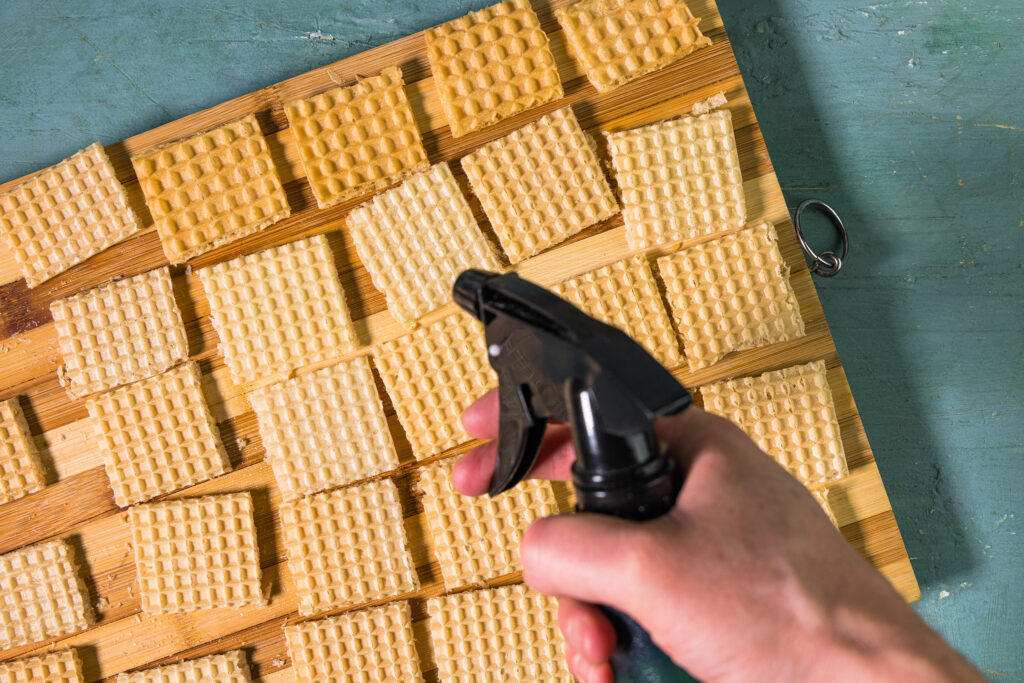Viereckige Waffeln und eine Hand mit einem Zerstäuber.