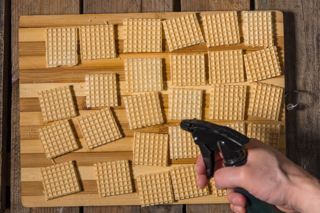 Eine Hand mit einem Zerstäuber befeuchtet Waffelvierecke.
