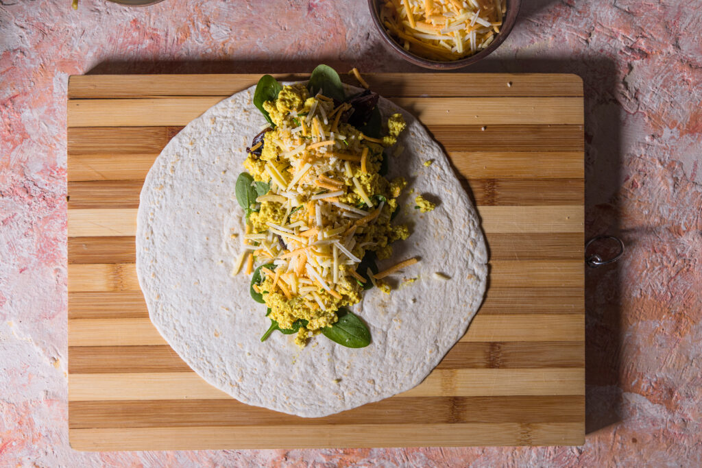 Den Tortilla Wrap mit Scrambled Tofu und veganem Streukäse belegen. Ich habe noch Spinat und gebratene Champignons hinzu gefügt.