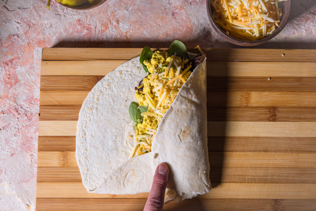 Ein belegter Soft Flour Tortilla, der gerade eingeklappt und aufgerollt wird.