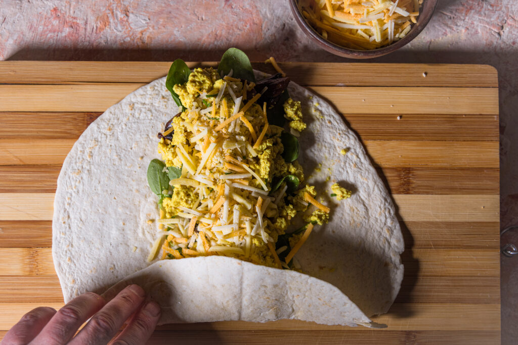 Ein belegter Soft Flour Tortilla, der gerade eingeklappt und aufgerollt wird.