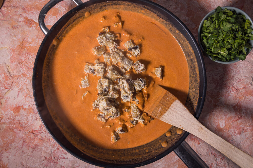 Marinierter, gebratener Seitan wird in eine Pfanne mit Tikka Sauce gegeben.