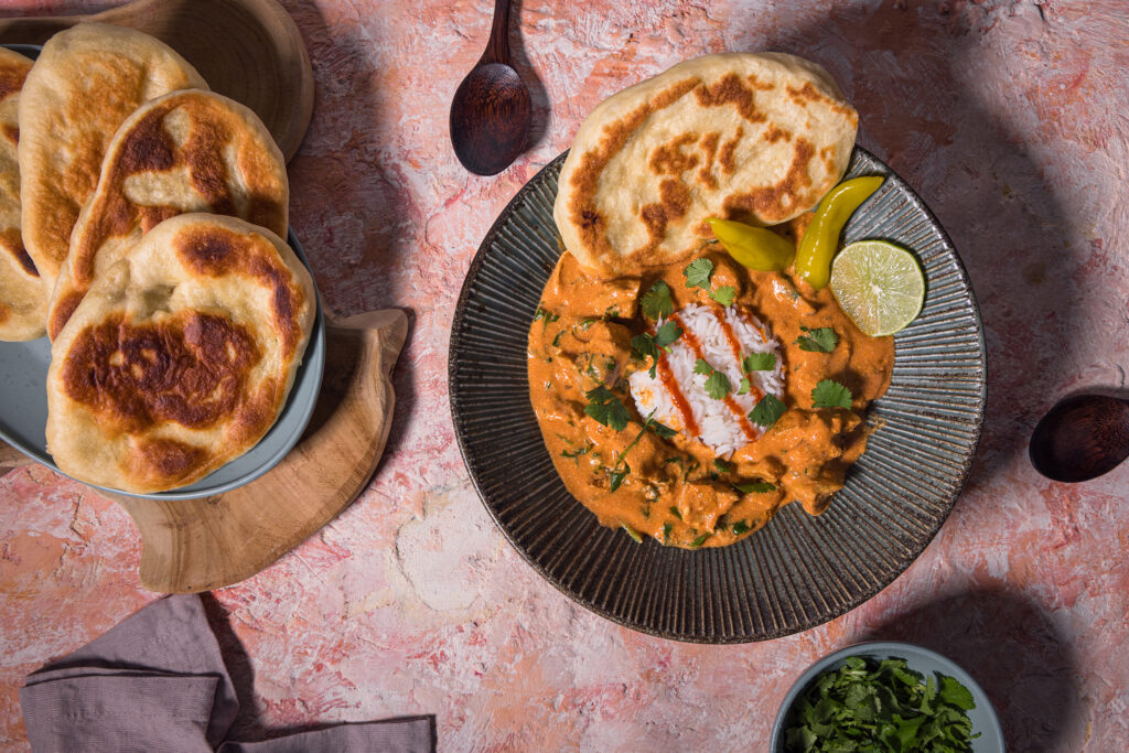 Seitan Tikka Masala und Naan auf Tellern auf einem rosa Tisch.