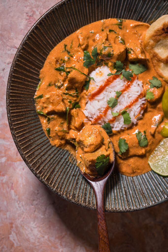 Veganes Chicken Tikka Masala mit Reis und Naan in einer Bowl. Darin ein gefüllter Löffel.