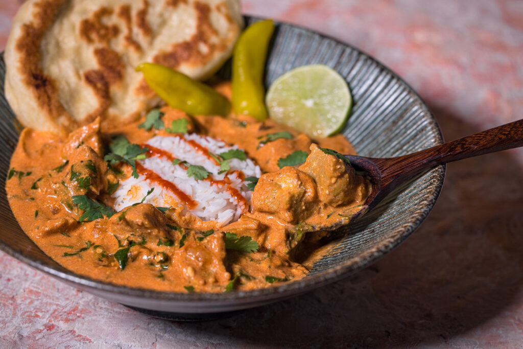 Seitan Tikka Masala mit Naan und Rein in einer Bowl. Ein Holzlöffel löffelt einen großen Happen heruas.