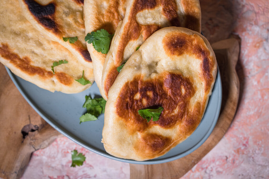Mehrere Naan auf einem Teller. Garniert mit Koriander.