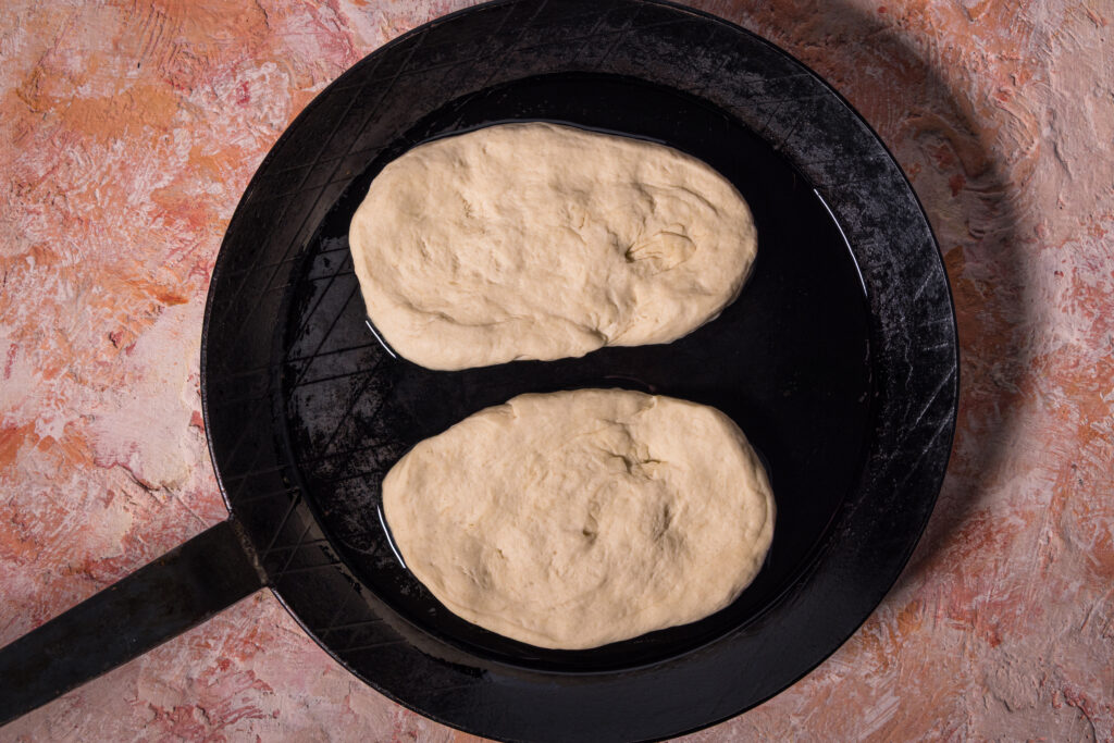 Zwei rohe Teigfladen werden zu Naan in einer Pfanne gebraten.
