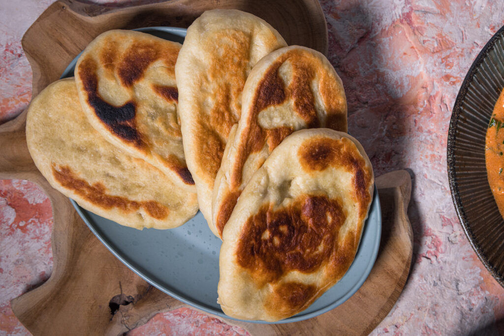 Mehrere Naan auf einem Teller. Garniert mit Koriander.