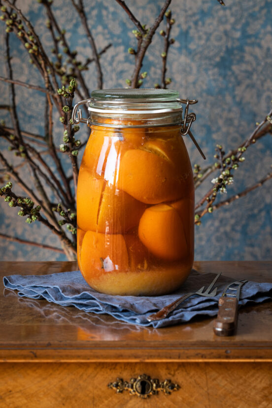 Salzorangen - laktofermentierte, eingelegte Orangen in einem großen Glas auf einem antiken Tisch