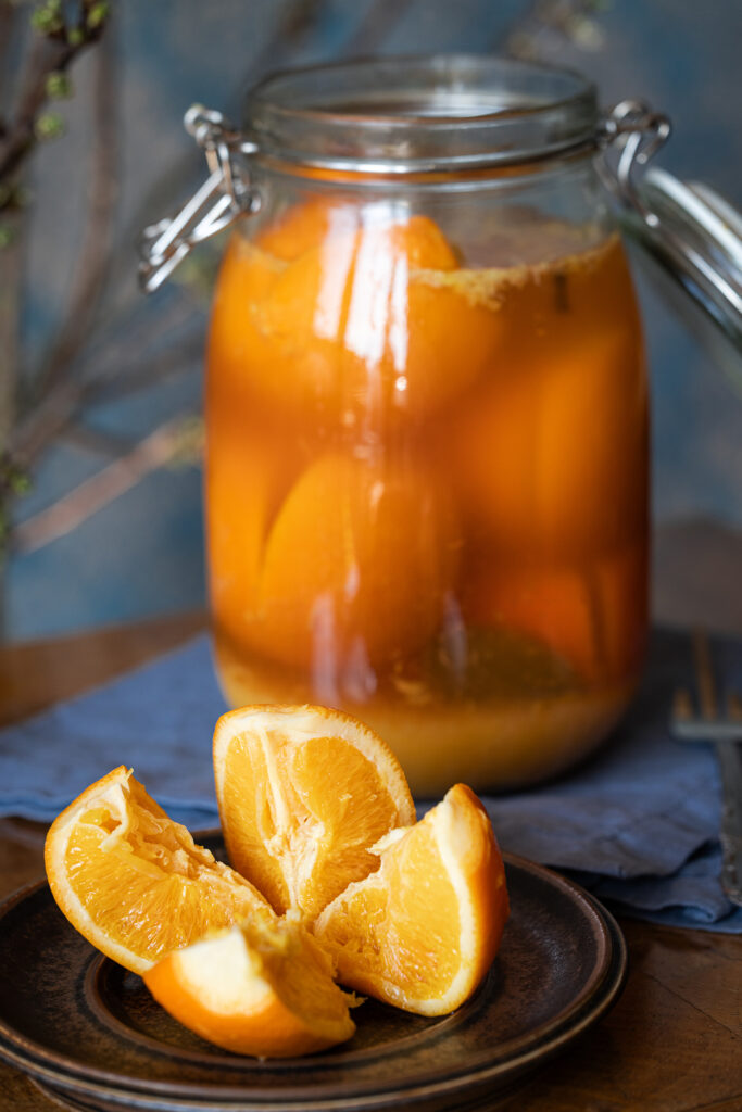 Salzorangen - laktofermentierte, eingelegte Orangen in einem großen Glas und auf einem Teller auf einem antiken Tisch