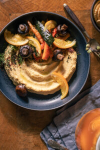 Salzorangen-Hummus - mit selbst eingelegten Salzorangen - auf einem schwarzen Teller mit Grillgemüse