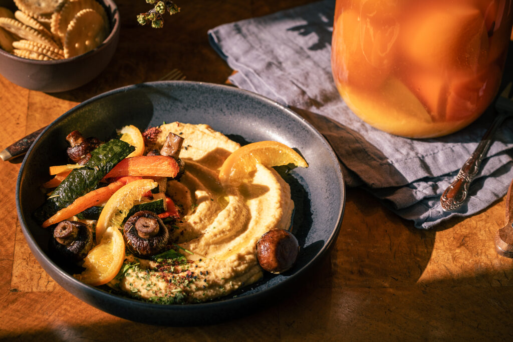 Salzorangen-Hummus mit Grillgemüse auf einem schwarzen Teller auf einem antiken Tisch