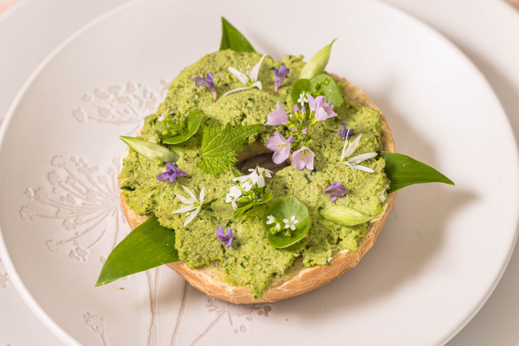 Bärlauchstreich mit Sonnenblumenkernen - auf einem Bagel mit essbaren Blütem