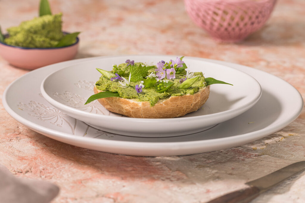 Bärlauchaufstrich auf einem Bagel auf einem rosa-roten Tisch.