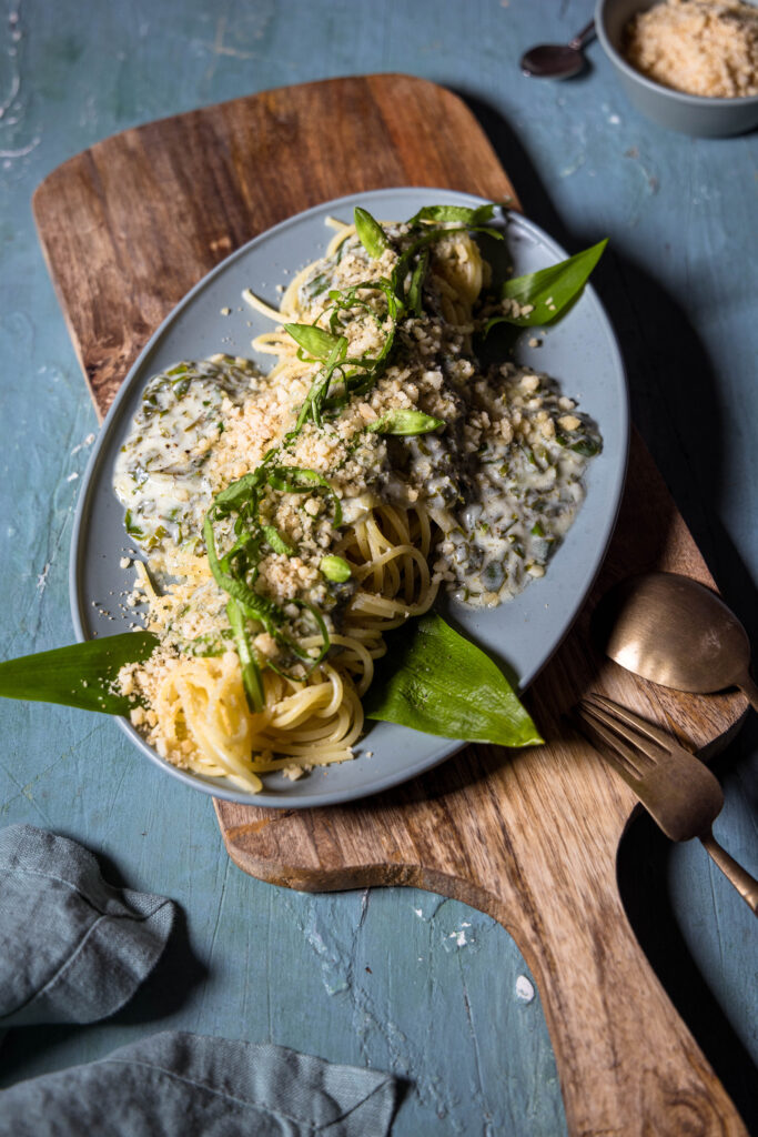Limetten Bärlauch Spaghetti mit Macadamia Parmesan auf einem grünen Teller auf einem Holzbrett.