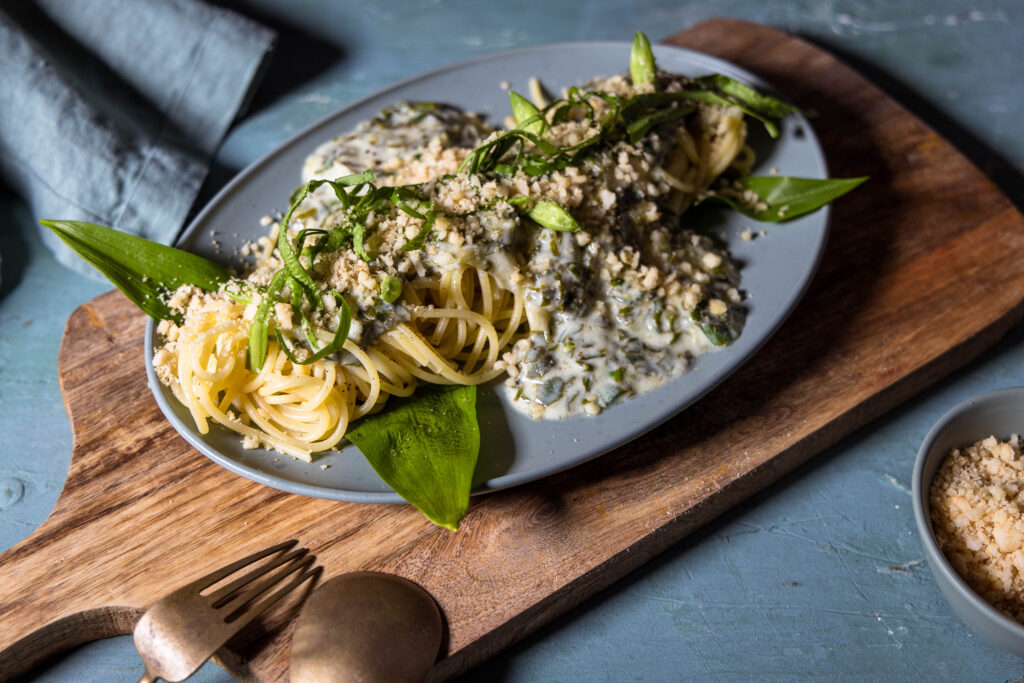 Limetten Bärlauch Spaghetti mit Macadamia Parmesan. Mit frischem Bärlauch garniert auf einem Teller.