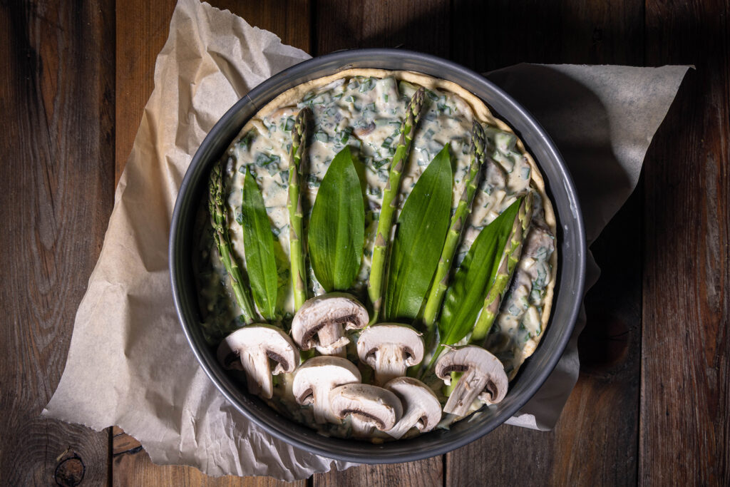 Eine rohe vegane Quiche, garniert mit Bärlauch, Spargel und Champignons.