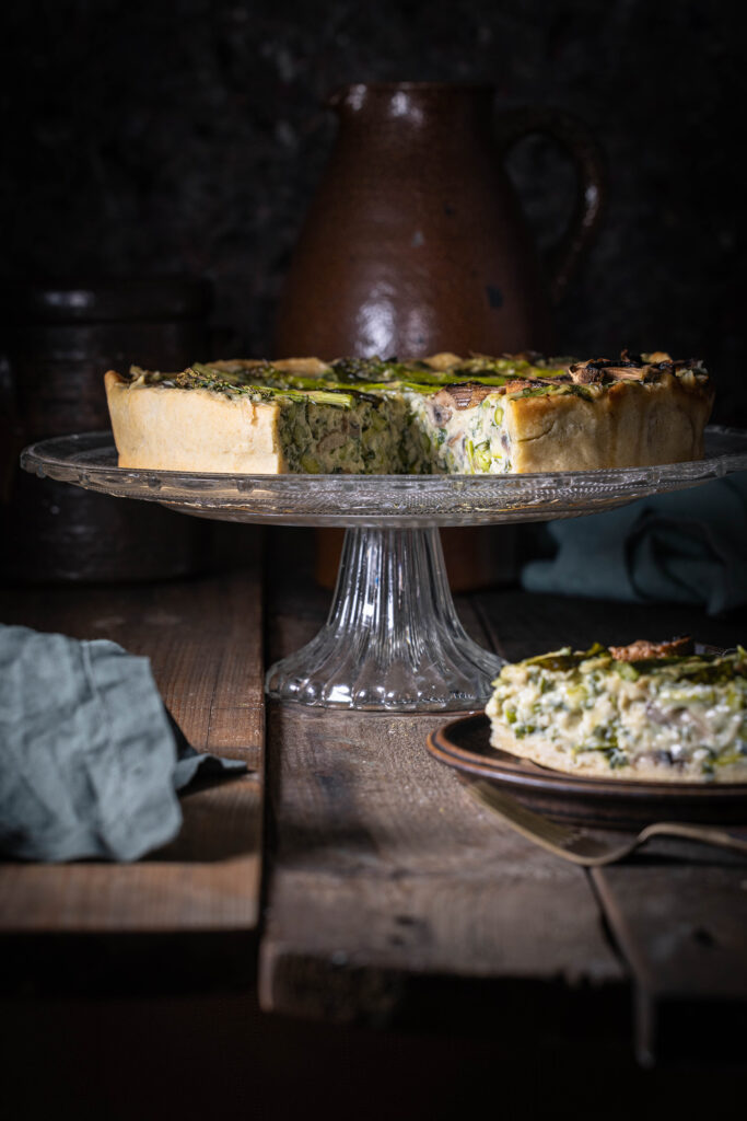 Vegane Bärlauchquiche mit grünem Spargel und Champignons auf einem antiken Holztisch