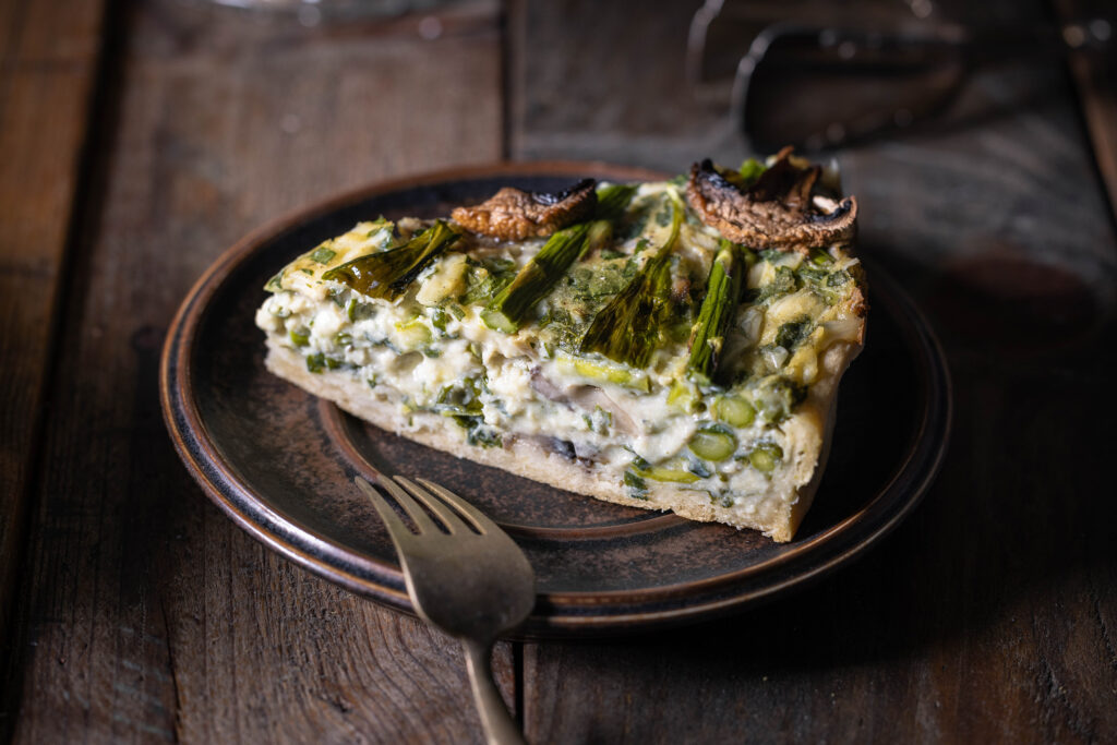 Ein Stück vegane Bärlauchquiche mit grünem Spargel und Champignons