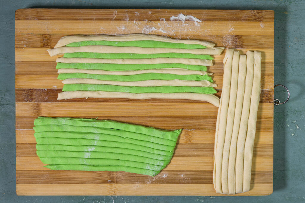 Ein grüner und ein weißer Ravioliteig, in dünne Streifen geschnitten. Die Streifen werden abwechselnd aneinander gelegt.