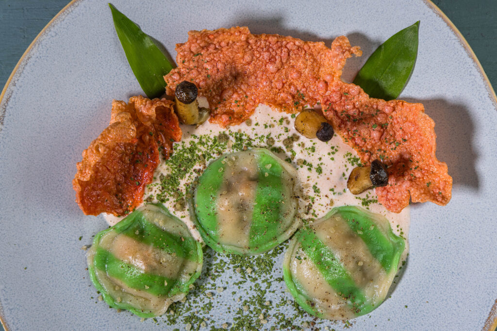Selbstgemachte Bärlauch-Ravioli auf hellem Tomatenschaum. Angerichtet mit Grünkohlpulver, Rote Beete Crackern und Kräutersetilingen.