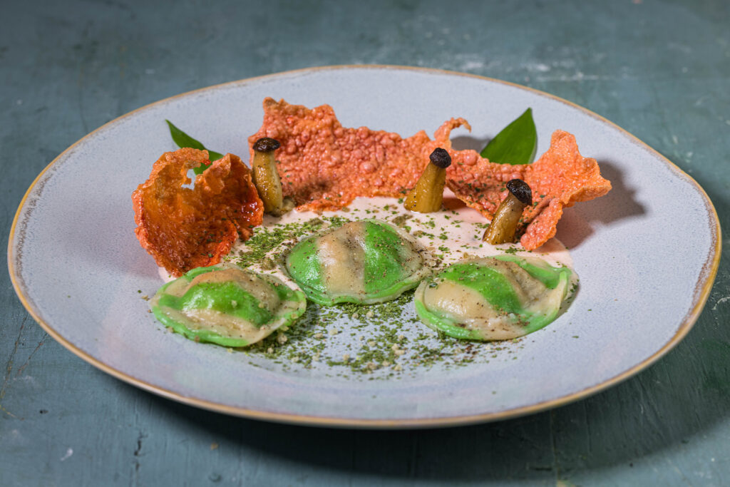 Selbstgemachte Bärlauch-Ravioli auf hellem Tomatenschaum. Angerichtet mit Grünkohlpulver, Rote Beete Crackern und Kräutersetilingen.