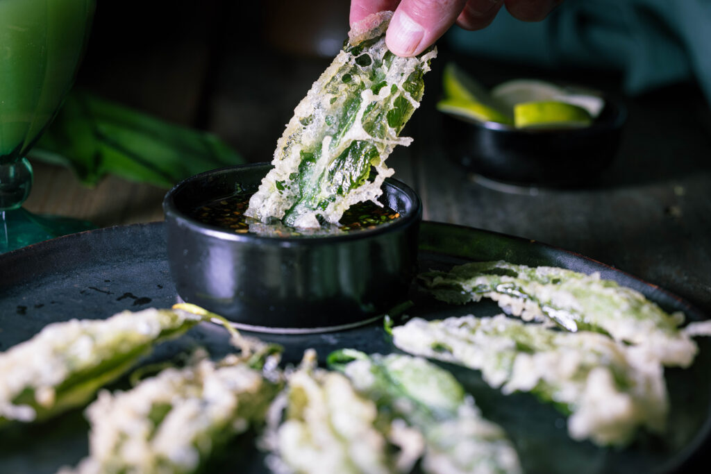 Eine Hand tunkt einen Bärlauch-Tempura in einen asiatischen Bärlauch-Dip