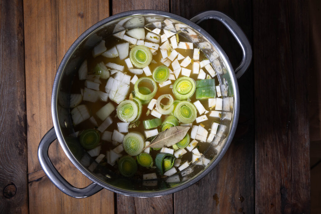 Suppe in einem Kochtopf, obenauf schwimmt Suppengemüse.