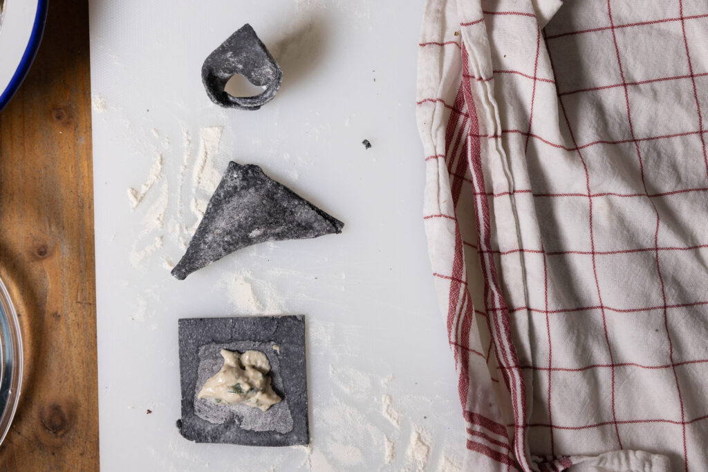 Vegane, schwarze Tortellini werden mit einer Bärlauch-Füllung gefüllt und geformt.