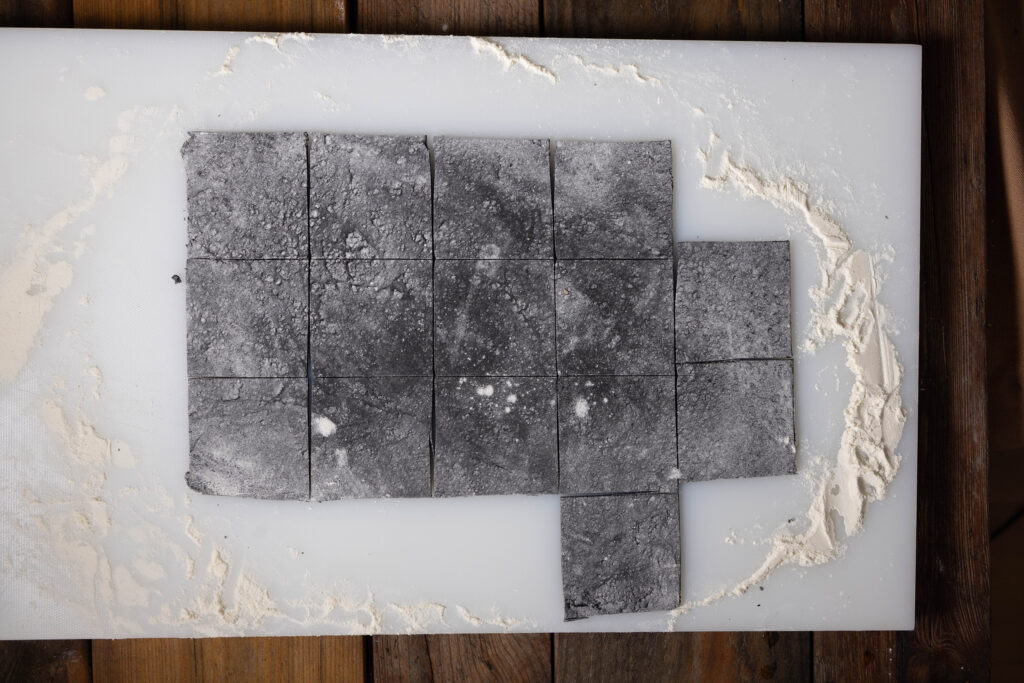 Ausgerollter, schwarzer Tortelliniteig, in Quadrate geschnitten.