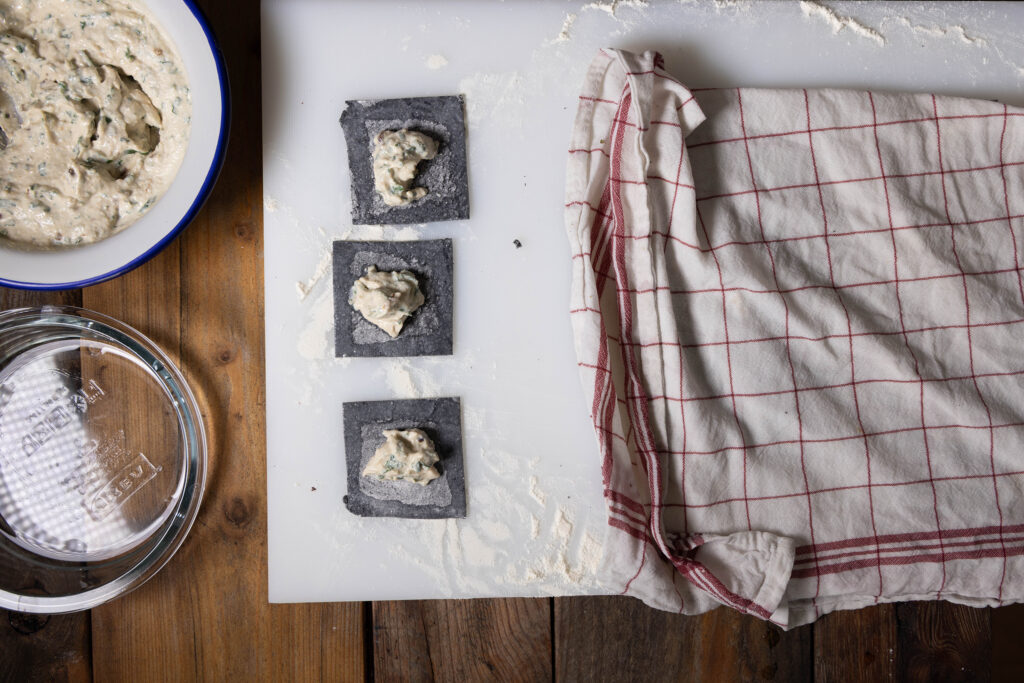 Vegane, schwarze Tortellini werden mit einer Bärlauch-Füllung gefüllt und geformt.