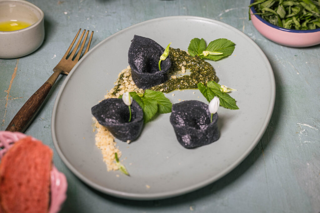 Gierschpesto mit laktofermentiertem Bärlauch auf einem Teller mit schwarzen Bärlauchtortellini und Macadamia Parmesan