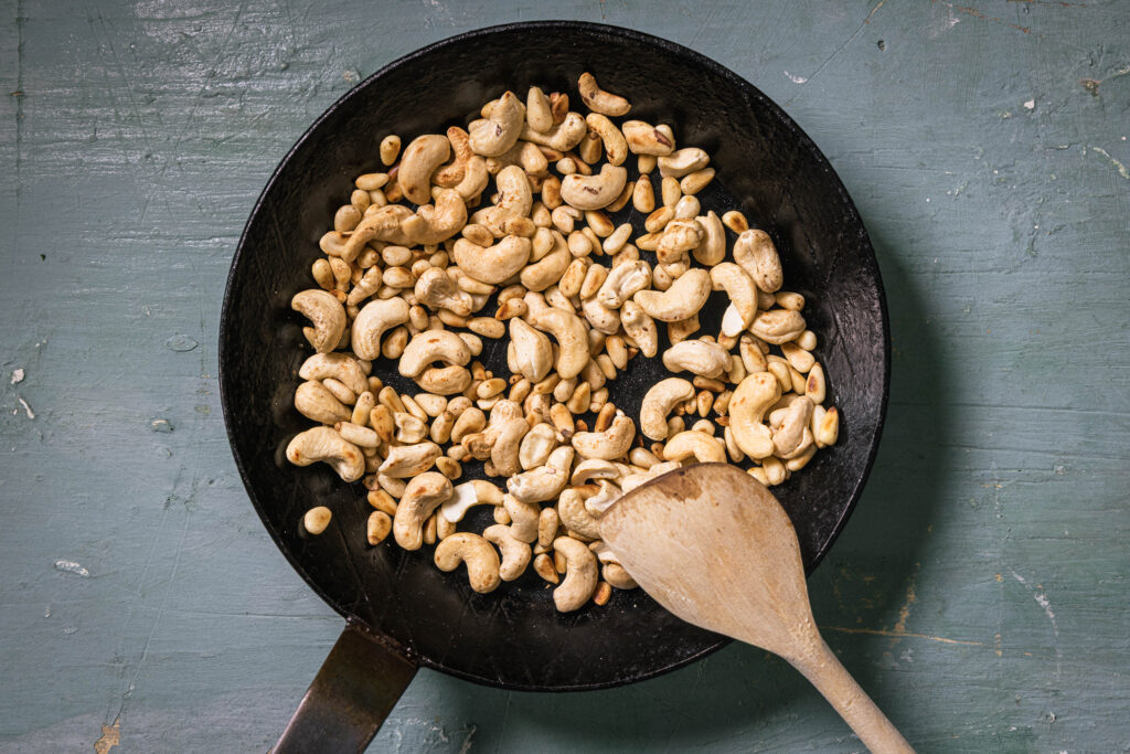 Cashews und Pinienkerne rösten ohne Fett in einer Pfanne.