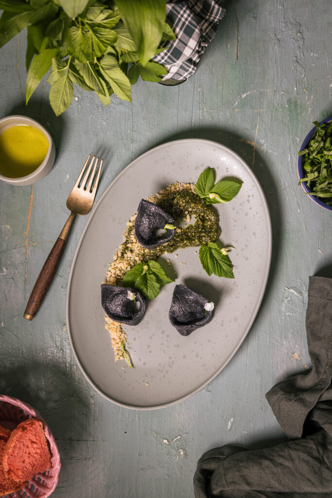 Gierschpesto mit laktofermentiertem Bärlauch auf einem Teller mit schwarzen Bärlauchtortellini und Macadamia Parmesan