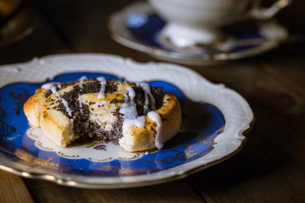 Vegane Mohnschnecken mit Hefeteig - angebissen auf einem blauen, antiken Teller. Im Hintergrund eine Sammeltasse.