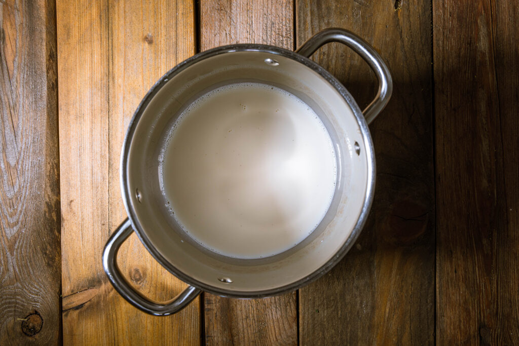 Sojamilch, Wasser, Salz, Vanillezucker und Zucker in einem großen Topf auf einem Holztisch.