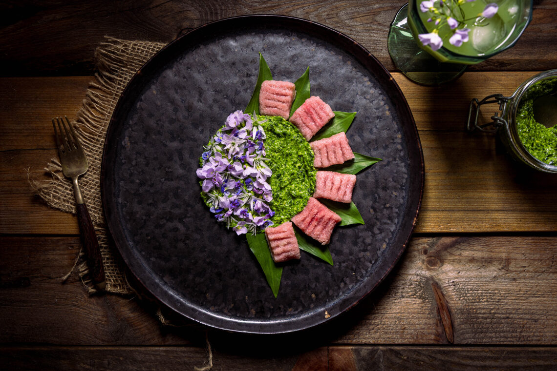 Selbstgemachte Rote Beete Gnocchi mit aromatischen Bärlauchpesto, mit essbaren Blüten angerichtet.