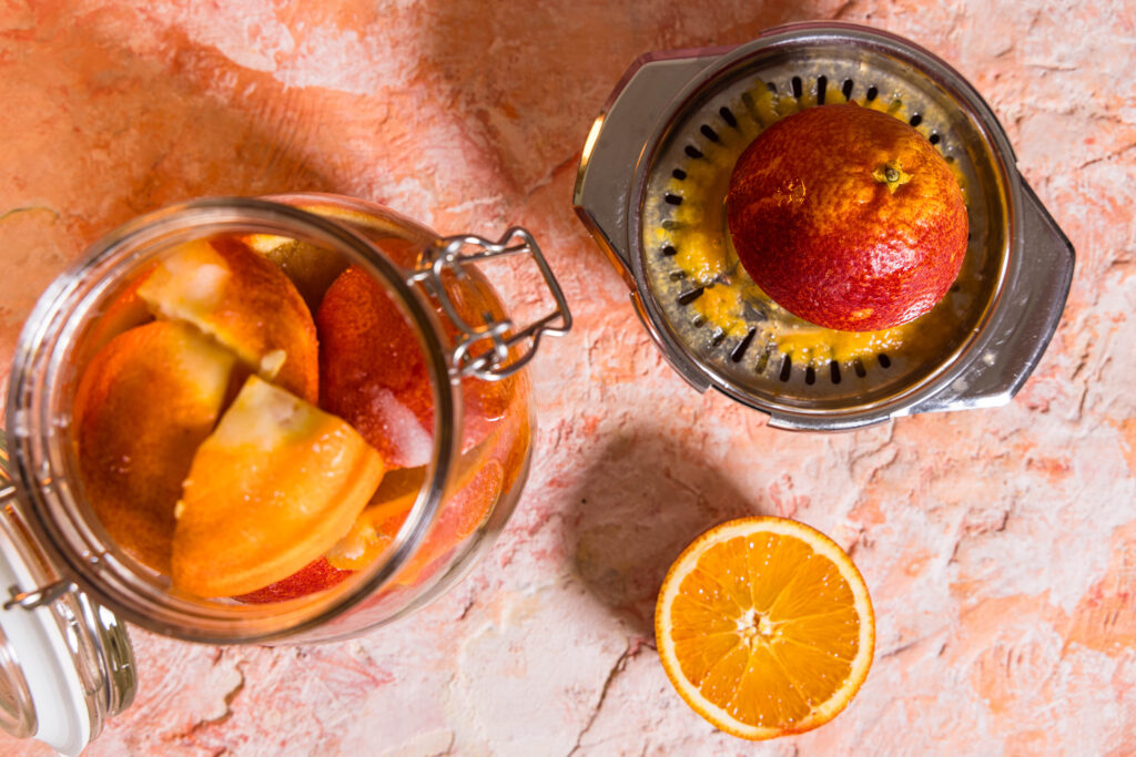Orangen in einem Glas, eine Orange wird gerade ausgepresst.