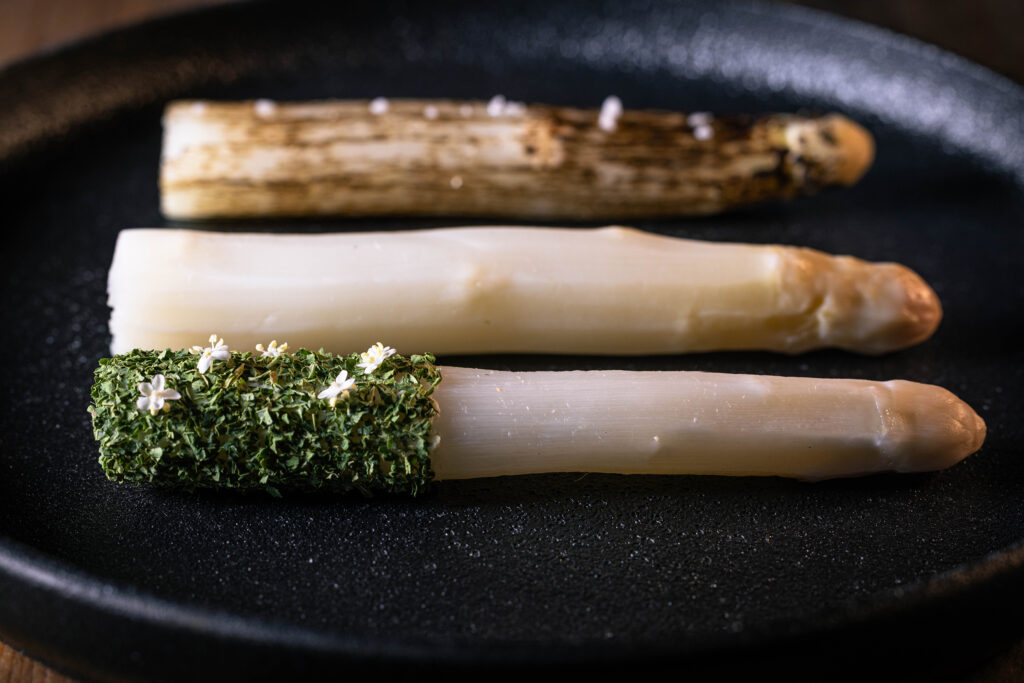 Dreierlei Spargel anrichten - hier mit Grünkohlpulver und Holunderblüte an der fermentierten Sragelstange.