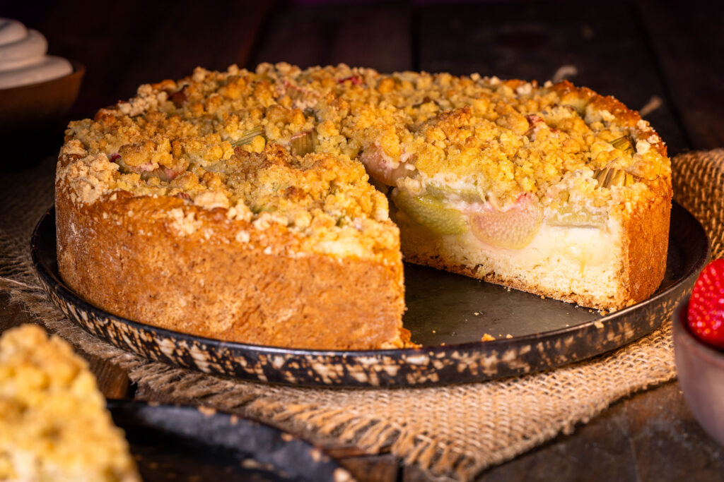 Rhabarberkuchen mit Streuseln und Puddingfüllung. Der ganze Kuchen, ein Stück ist heraus geschnitten.