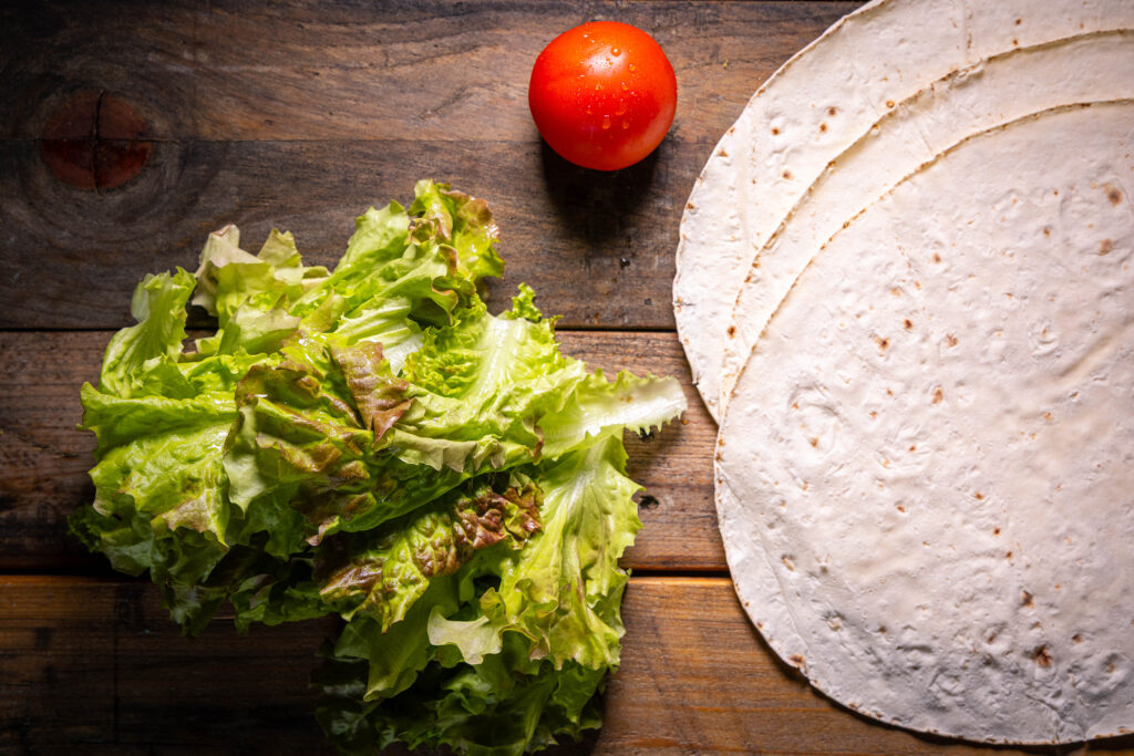 Lavash-Brote, eine Tomate und frischer Salat auf einem alten Holztisch.
