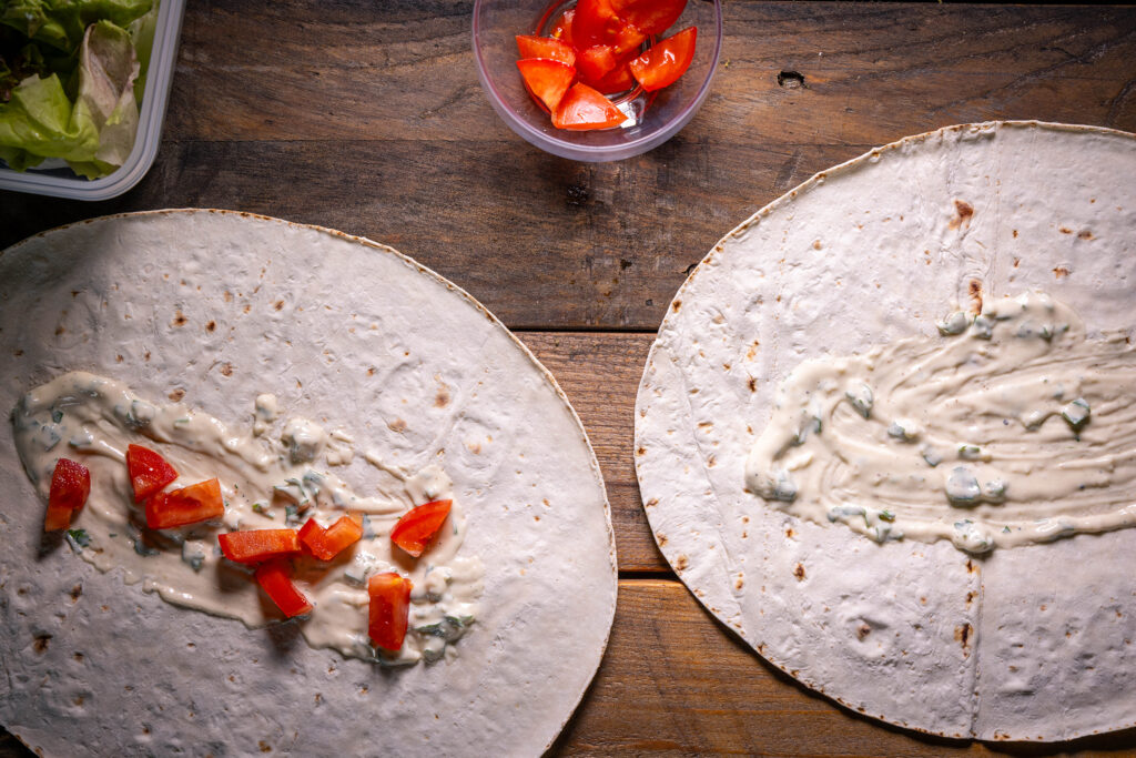 Die Lavash-Fladen mit Joghurt-Tahini-Sauce bestrichen, einer ist mit Tomatenwürfeln belegt.