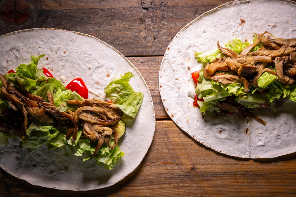 Vegane Schawarma werden mit Sauce, Tomaten, Salat, Grillgemüse und Austernpilz-Schawarma-Fleisch belegt.
