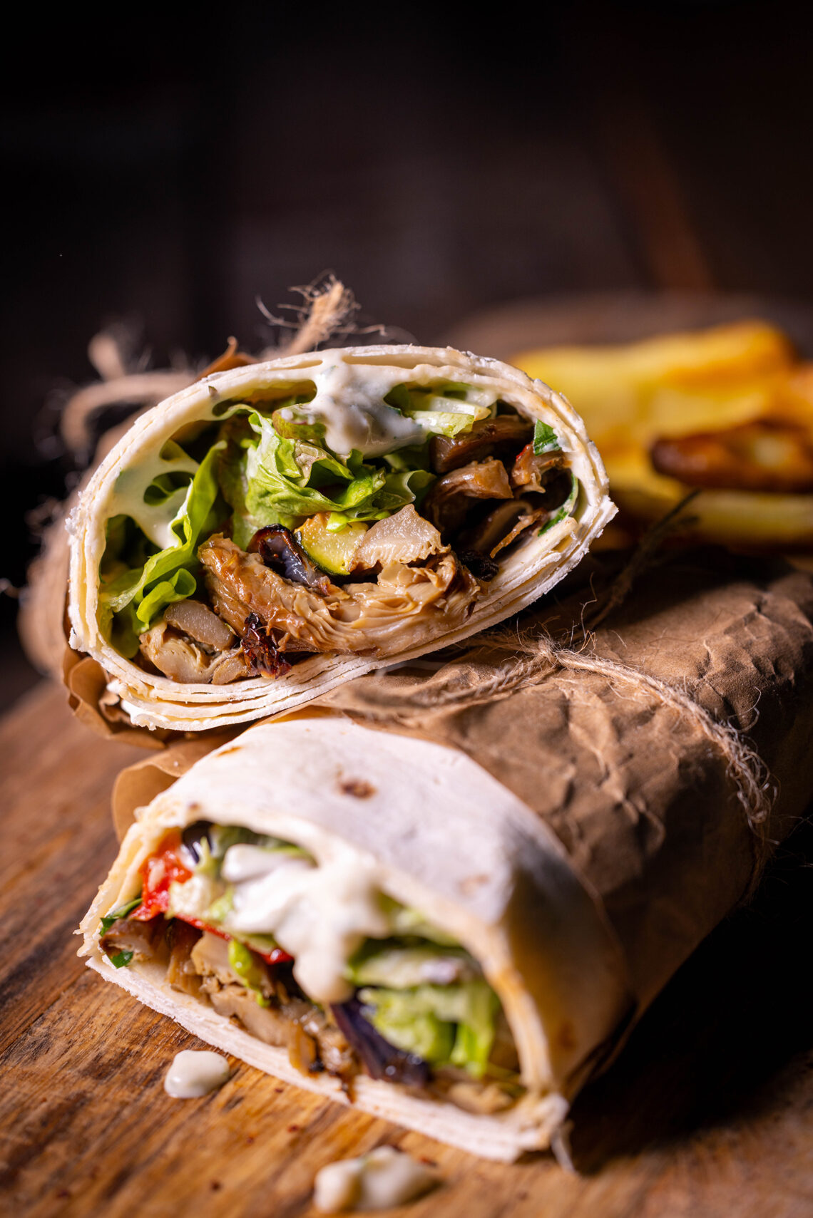 Vegane Schawarma aus Austernseitlingen mit Grillgemüse. Auf einem Holzbrett mit Pommes im HIntergrund.