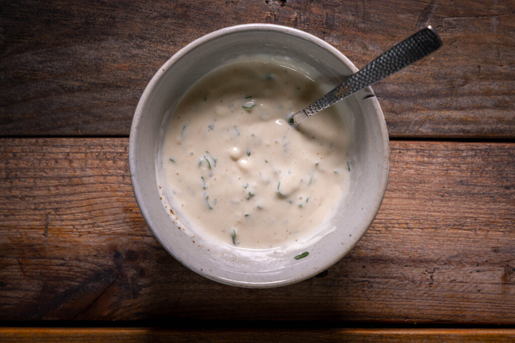 Vegane Joghurt-Tahini-Sauce in einer Schale auf einem alten Holztisch.
