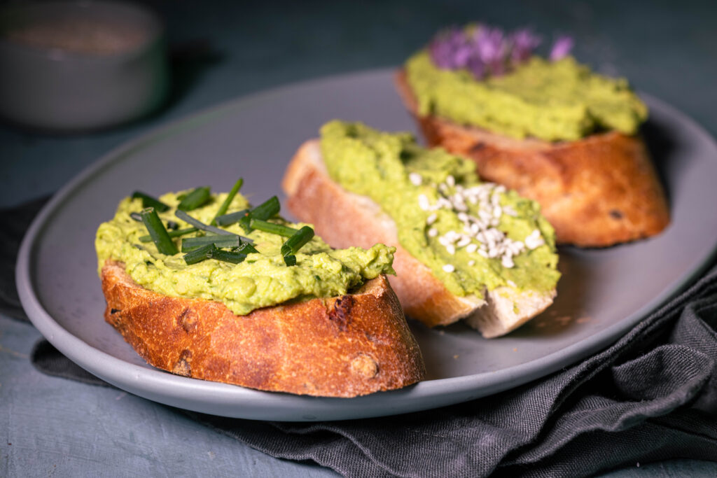 Drei Scheiben Baguette, dick belegt mit Schnittlauch-Hummus. Verschieden garniert.