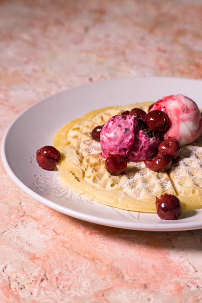 Waffeln schmecken mit vielen süßen Toppings. Hier mit zwei Sorten Eis, Puderzucker und eingekochten Kirschen.