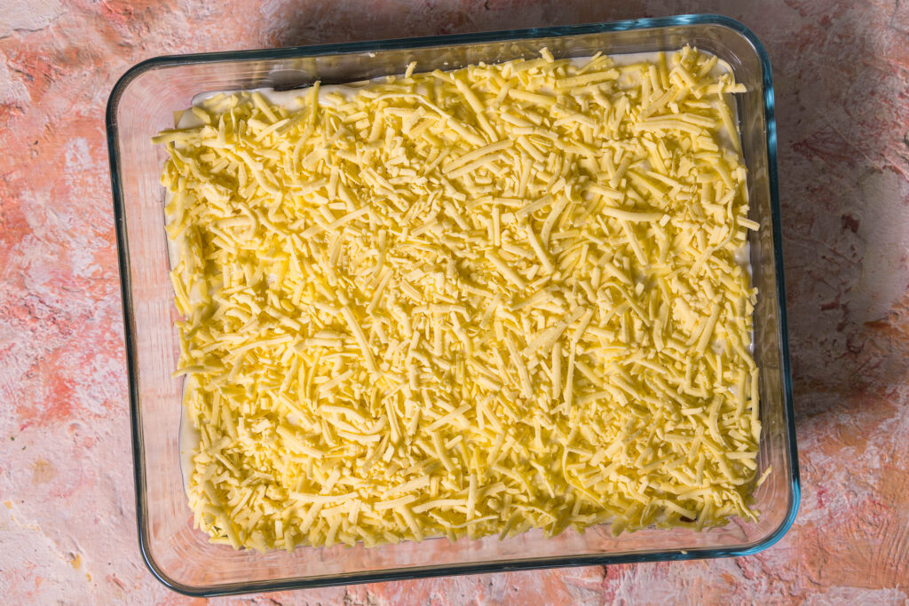 Eine vegane Wildkräuterlasagne wird in einer Auflaufform geschichtet.