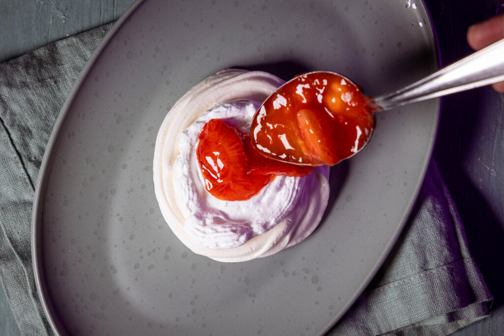 Erdbeerkpompott wird auf die Sahne in einem Pavlova gegeben.