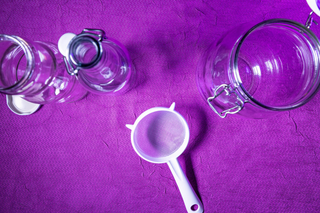 Flaschen, ein Plastiksieb und ein Gärgefäß (ein großes Glasgefäß).